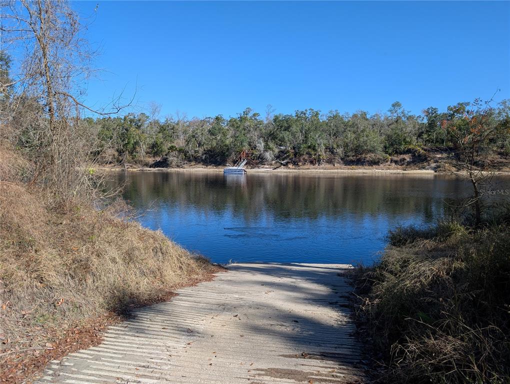 A concrete boat ramp leads into a calm river surrounded by trees under a clear sky — NW FOX RUN TRAIL UNIT 107, MAYO, FL