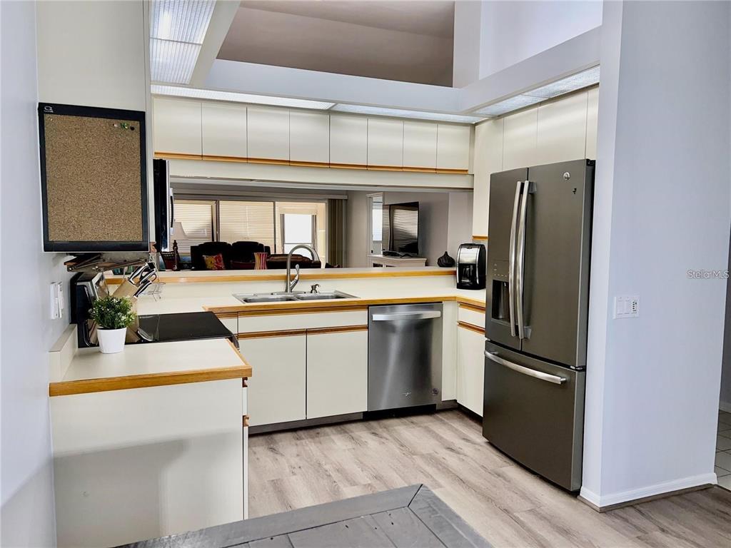 A kitchen features white cabinets with wood trim, stainless steel appliances, and light wood flooring — 7186 LAKESIDE DRIVE, SARASOTA, FL