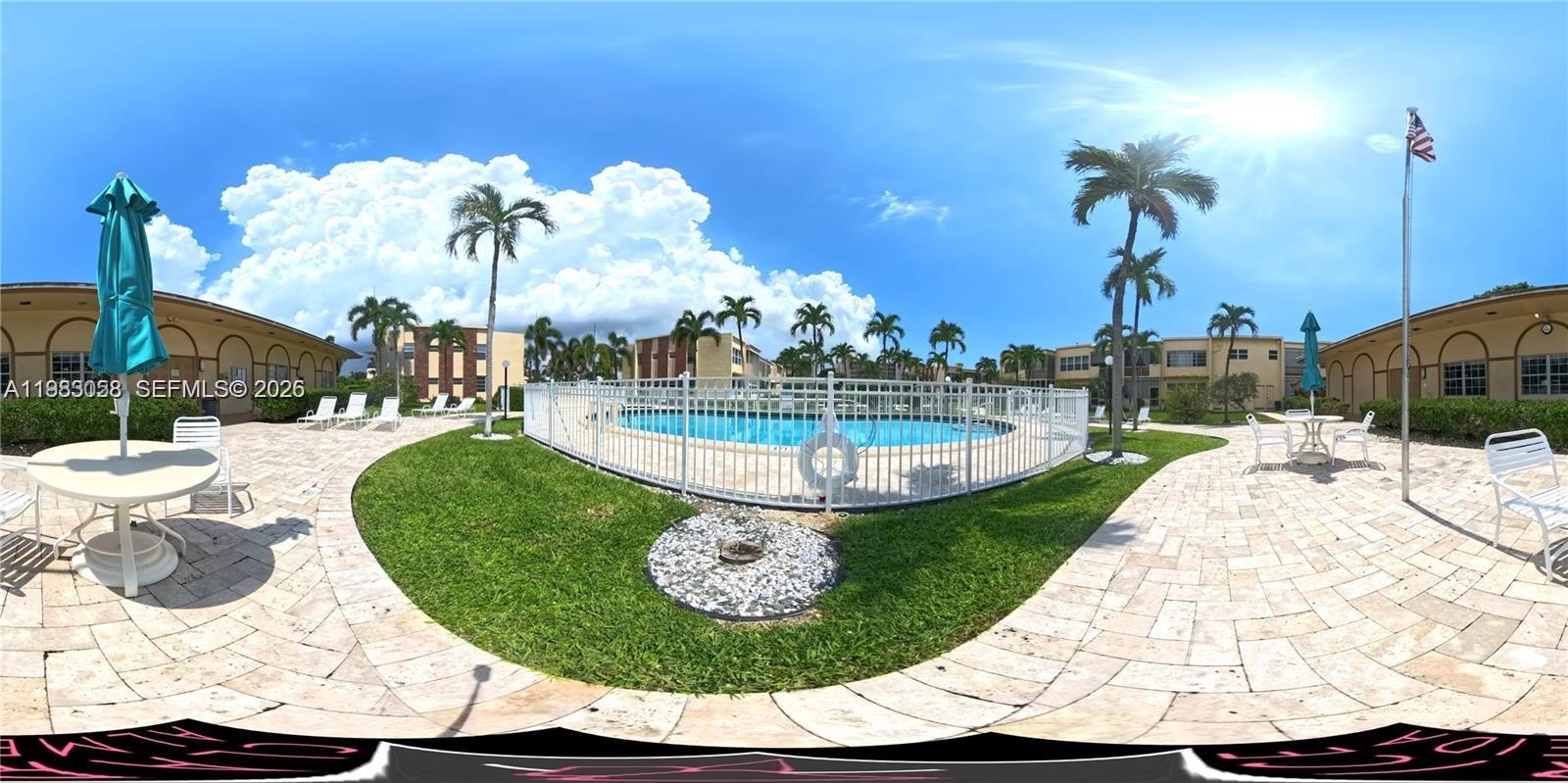 A swimming pool is enclosed by a white fence on a paved patio with palm trees — 851 NE 14th Ave # 414, Hallandale Beach FL 33009, HALLANDALE BEACH, FL