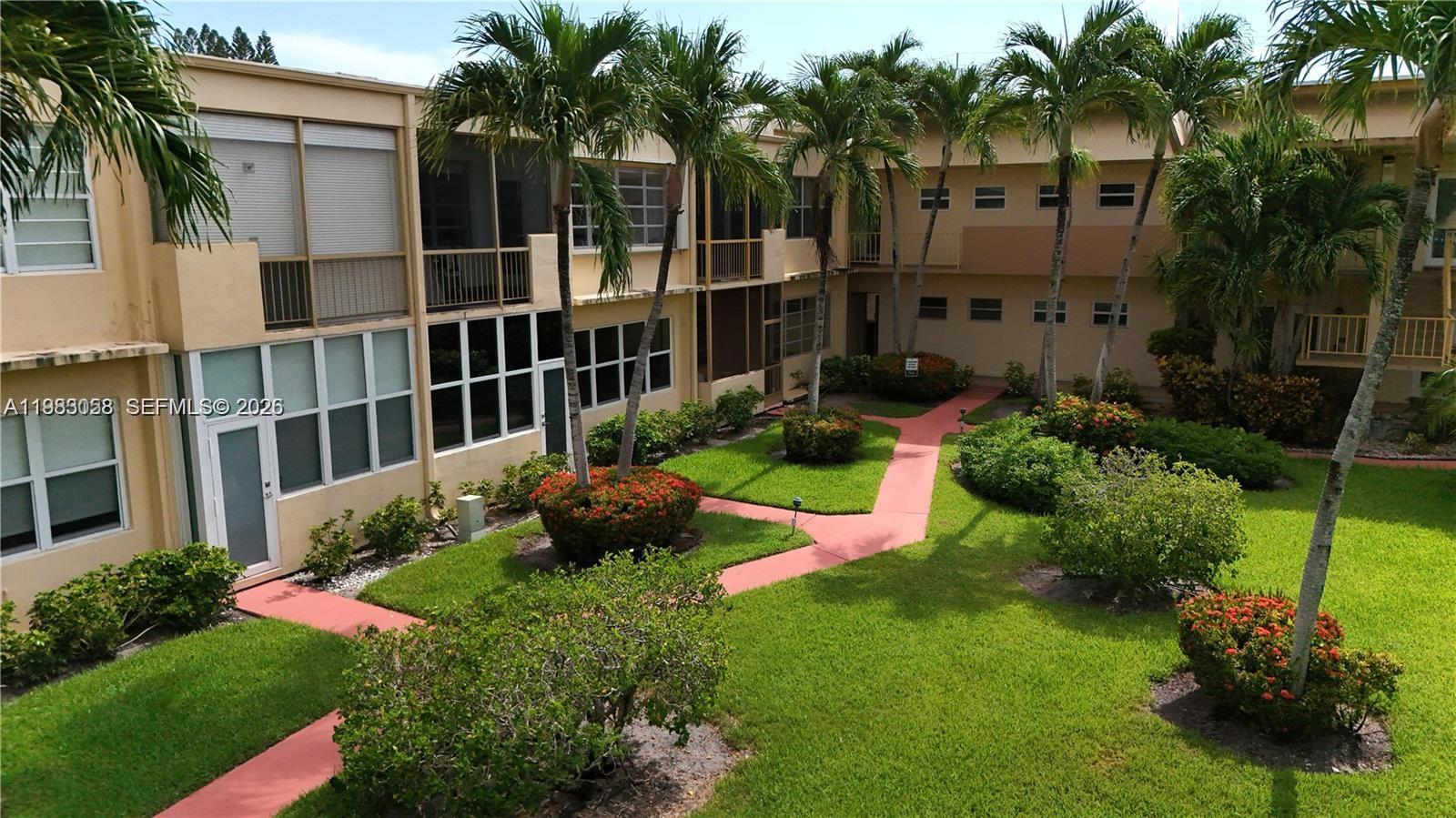 An exterior view of a two-story apartment complex with a courtyard and palm trees — 851 NE 14th Ave # 414, Hallandale Beach FL 33009, HALLANDALE BEACH, FL