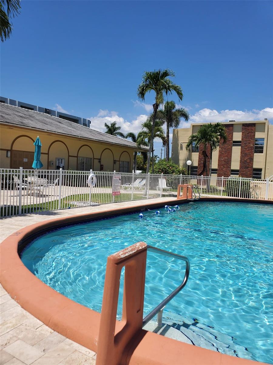 A swimming pool with a terracotta-colored edge sits in front of a multi-story apartment building — 851 NE 14th Ave # 414, Hallandale Beach FL 33009, HALLANDALE BEACH, FL