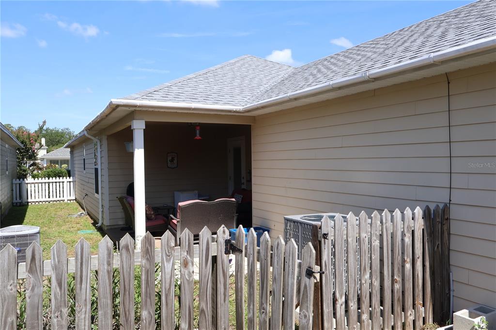 A tan house features a covered patio, a wooden fence, and an outdoor air conditioning unit — 3803 NW 26TH STREET, GAINESVILLE, FL