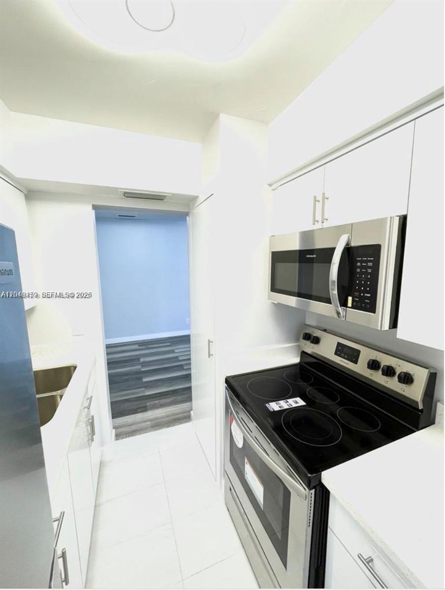 A galley-style kitchen features white cabinets, stainless steel appliances, and light-colored tile flooring — 1431 S 14th Ave # 208, Hollywood FL 33020, HOLLYWOOD, FL