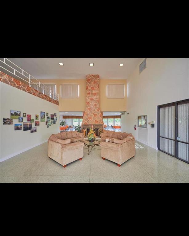 A spacious lobby features a stone fireplace, two beige sofas, and a balcony overlooking the room — 1011 TROPICANA DRIVE, INDIAN LAKE ESTATES, FL