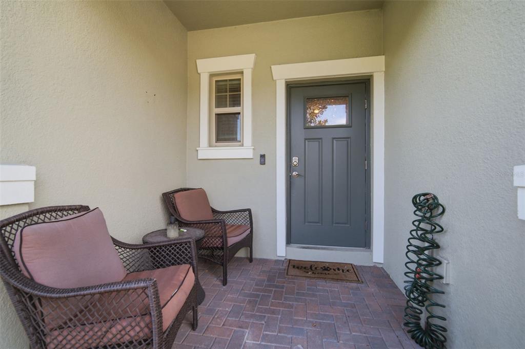 A covered entryway features a gray front door, two wicker chairs, and brick pavers — 21850 LYONIA LANE, LAND O LAKES, FL