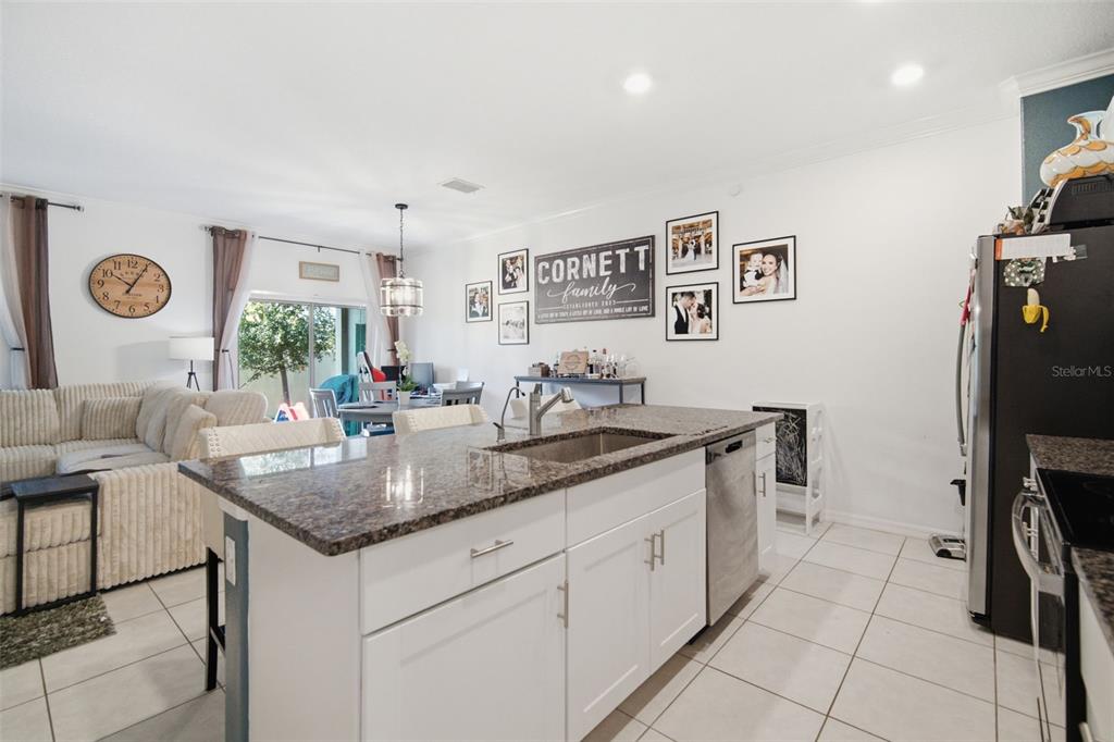 A kitchen island with a granite countertop sits in front of a living and dining area — 21850 LYONIA LANE, LAND O LAKES, FL