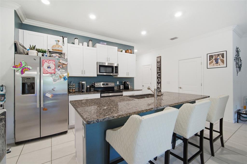 A kitchen features white cabinets, a granite-topped island with bar stools, and stainless steel appliances — 21850 LYONIA LANE, LAND O LAKES, FL
