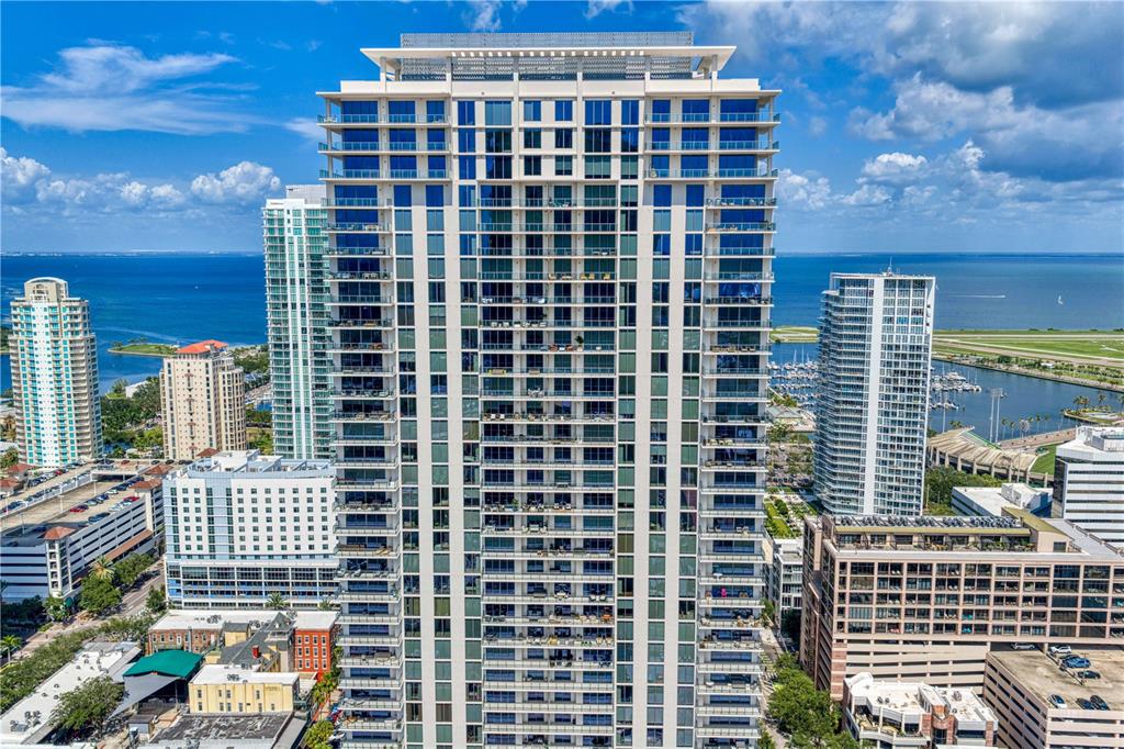 An aerial view of a tall residential skyscraper surrounded by other buildings and the bay — 275 1ST AVENUE S UNIT 3906, ST PETERSBURG, FL