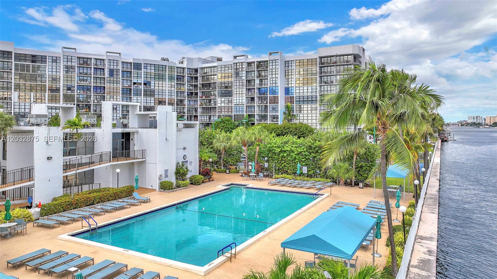An outdoor swimming pool is situated beside a large apartment building and a waterway — 1000 Parkview Dr # 229, Hallandale Beach FL 33009, HALLANDALE BEACH, FL