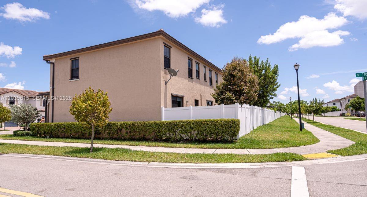 A two-story beige townhouse exterior features a white vinyl fence and a manicured hedge — 11064 W 33rd Way, Hialeah FL 33018, HIALEAH, FL