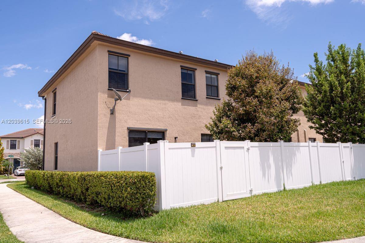 A two-story tan stucco house features a white vinyl fence enclosing a backyard area — 11064 W 33rd Way, Hialeah FL 33018, HIALEAH, FL