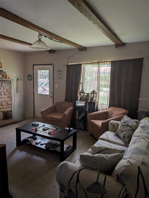 A living room features exposed ceiling beams, a stone fireplace, and a patterned sofa — 5610 WILSON ROAD, SANFORD, FL
