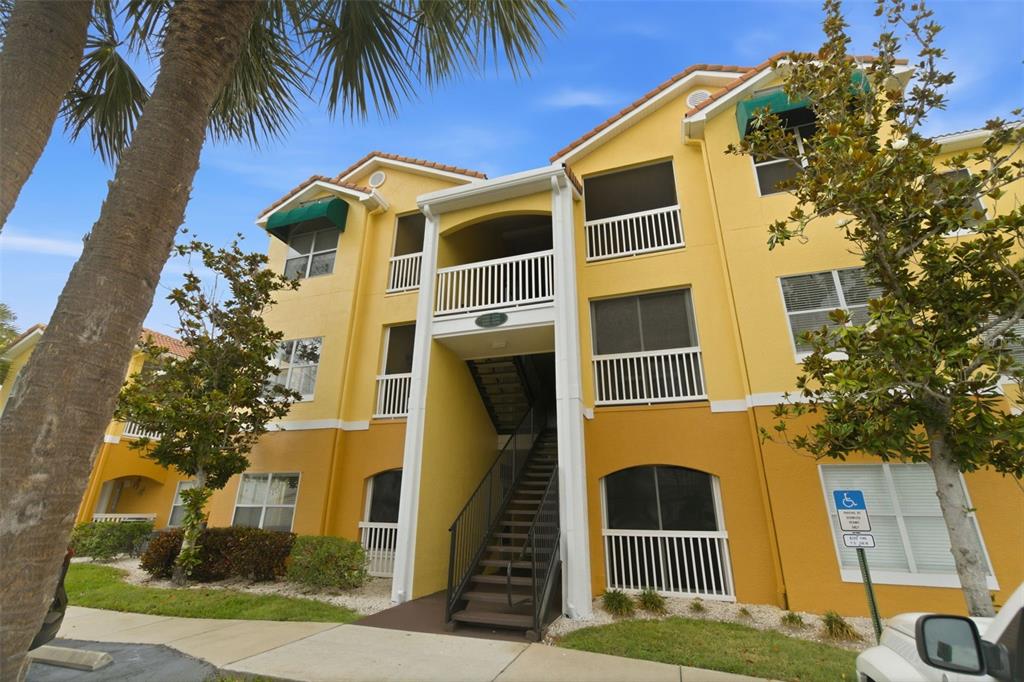 A three-story yellow apartment building features an exterior staircase and a palm tree — 10764 70TH AVENUE UNIT 6206, SEMINOLE, FL
