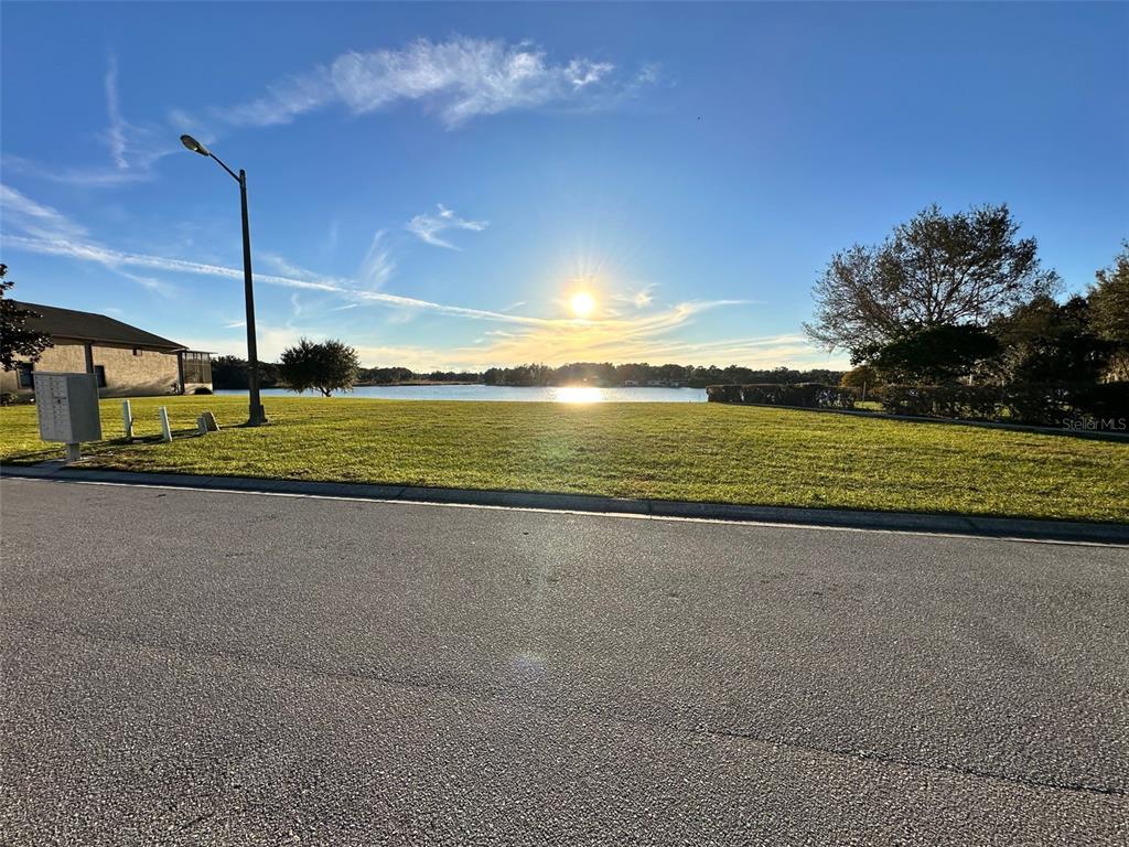 A grassy vacant lot overlooks a lake under a bright sun and blue sky — 528 MEANDERING WAY, POLK CITY, FL