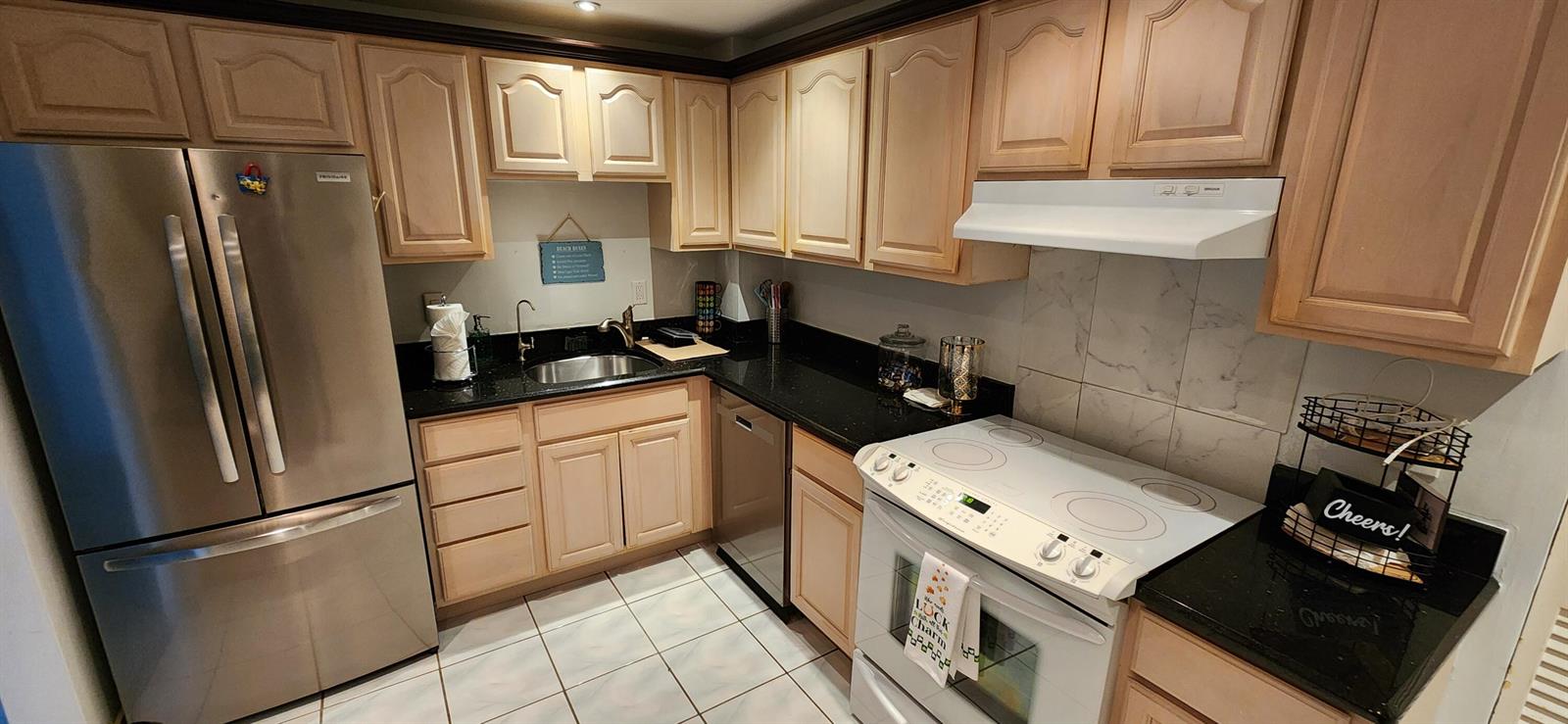 A kitchen with light wood cabinets, black countertops, stainless steel appliances, and white tiled floors — 405 N Ocean Boulevard # 1507, Pompano Beach FL 33062, POMPANO BEACH, FL