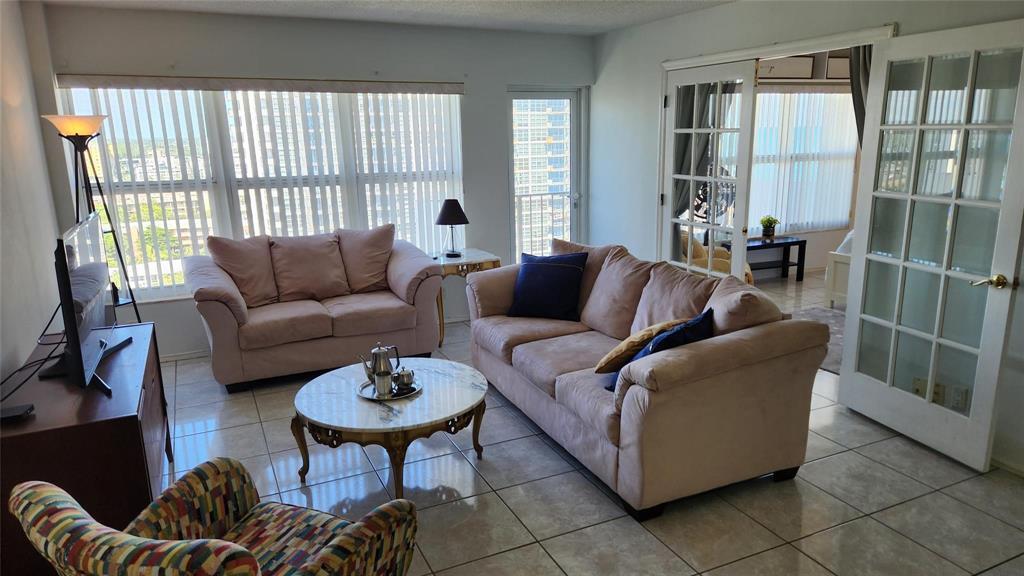 A living room features light-colored tile flooring, two beige sofas, a patterned armchair, and large windows — 405 N Ocean Boulevard # 1507, Pompano Beach FL 33062, POMPANO BEACH, FL