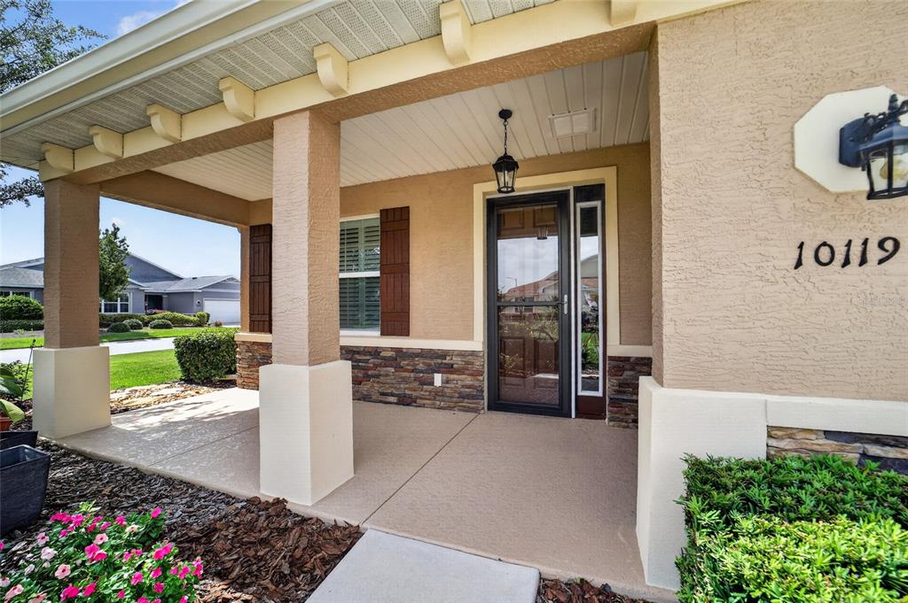 The front porch of a house features a stone-accented wall, a glass door, and columns — 10119 SW 88TH STREET, OCALA, FL