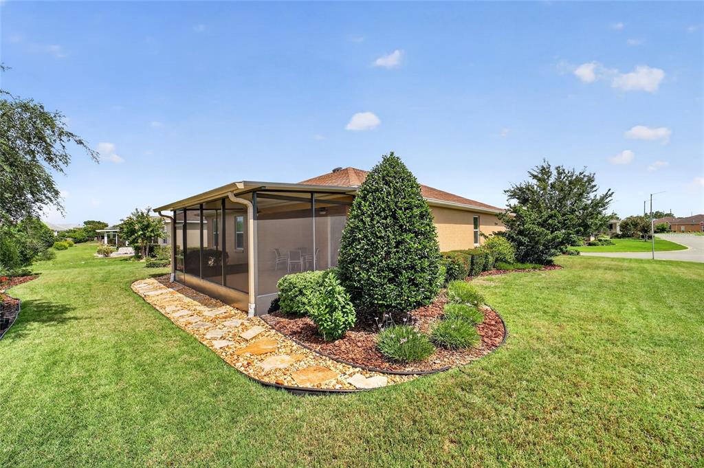 A tan house features a screened-in porch and a landscaped garden bed with stone pavers — 10119 SW 88TH STREET, OCALA, FL