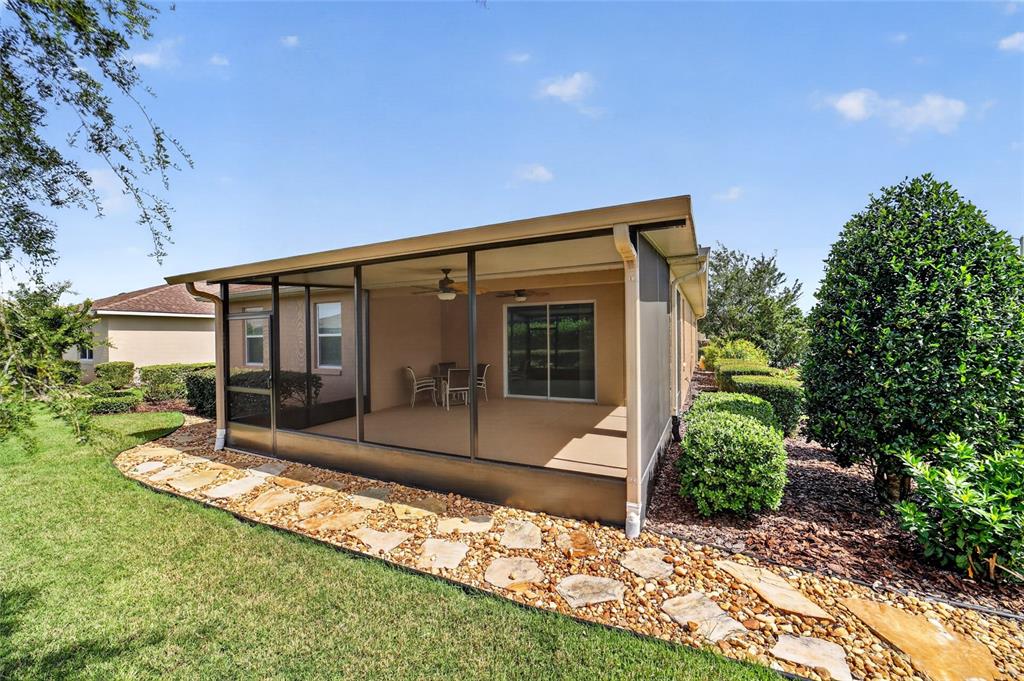 A screened-in patio with a stone walkway sits beside a house with manicured landscaping — 10119 SW 88TH STREET, OCALA, FL