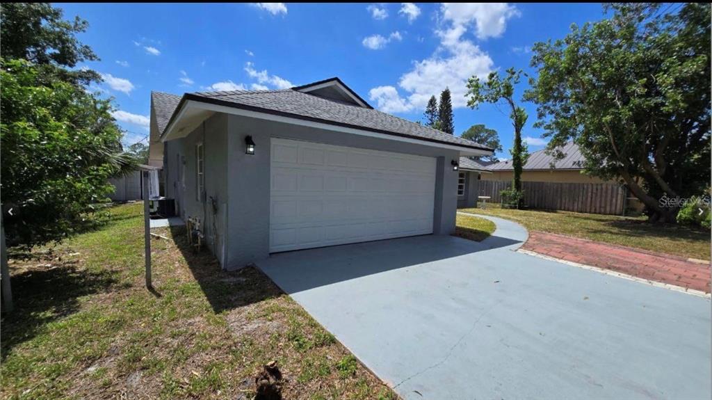 A gray house exterior features a white two-car garage door and a painted concrete driveway — 34 EMERSON DRIVE NW, PALM BAY, FL