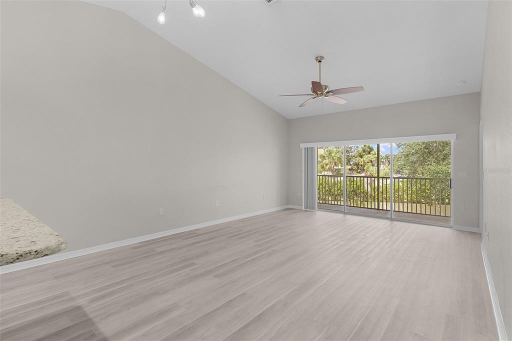 A bright living room features light wood-look flooring, vaulted ceilings, and a sliding glass door — 5308 BOWLINE COURT, OXFORD, FL