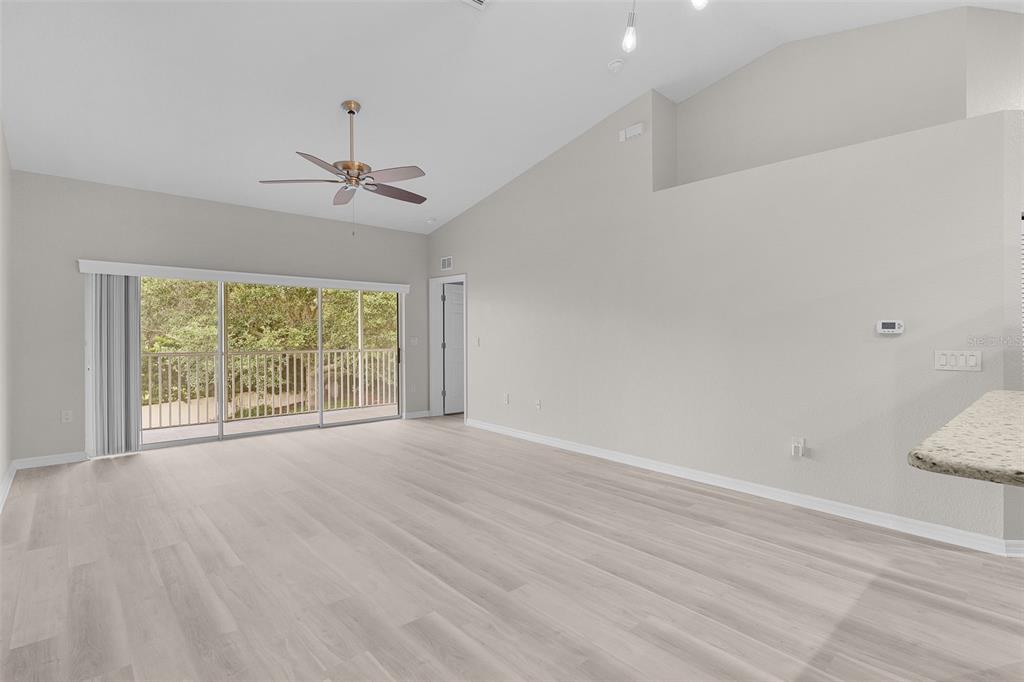 A spacious living room features light wood-look flooring, vaulted ceilings, and a sliding glass door — 5308 BOWLINE COURT, OXFORD, FL