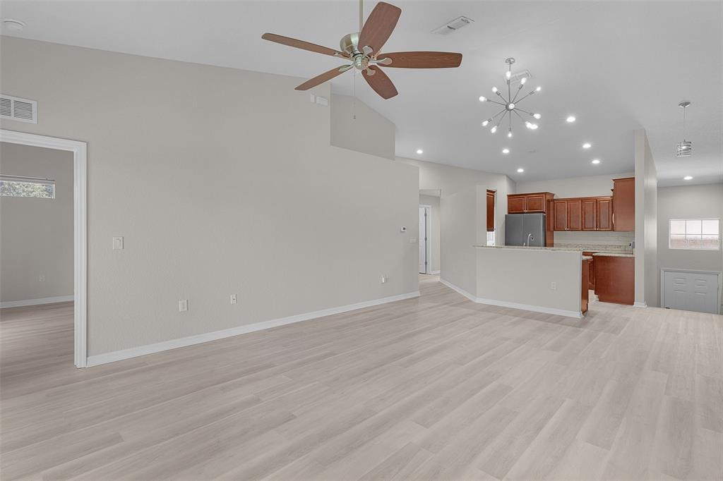 A spacious living room with light wood-look flooring, a ceiling fan, and an open kitchen — 5308 BOWLINE COURT, OXFORD, FL