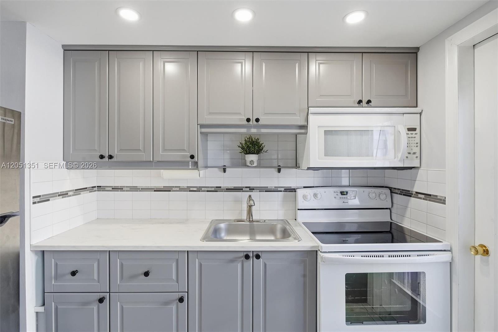 A kitchen features gray cabinets, white countertops, a white stove, and a tiled backsplash — 3133 S Ocean Dr # 218, Hallandale Beach FL 33009, HALLANDALE BEACH, FL