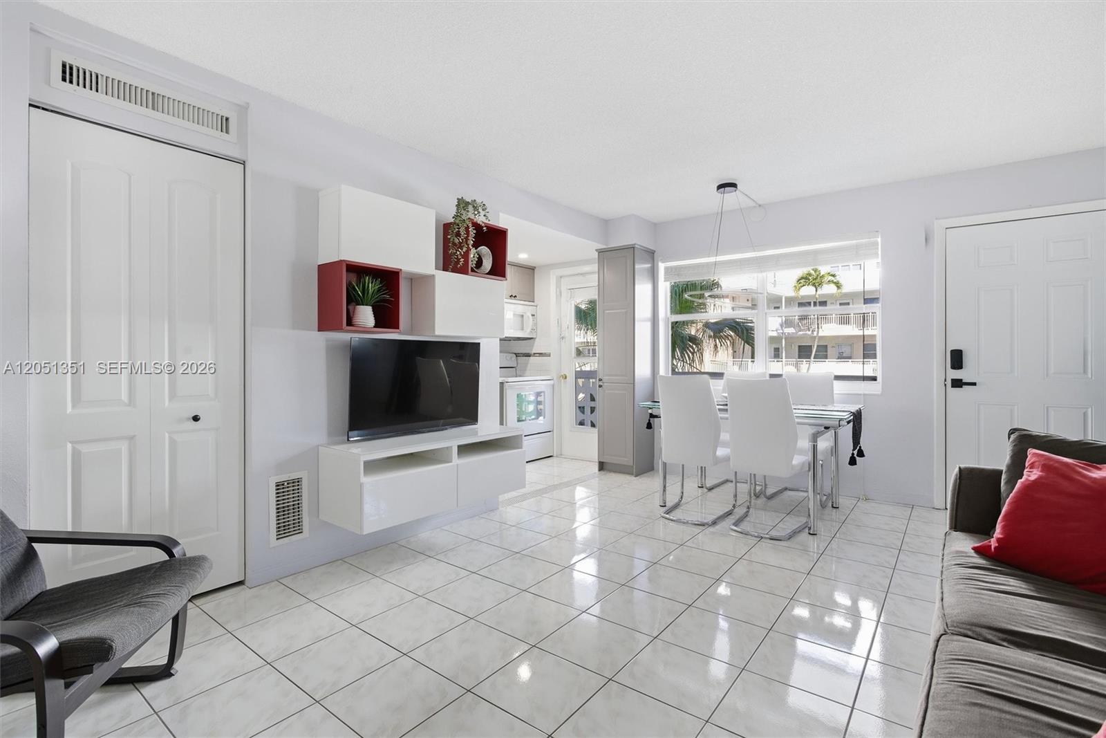 This living and dining area features white tile floors, a wall-mounted TV unit, and furniture — 3133 S Ocean Dr # 218, Hallandale Beach FL 33009, HALLANDALE BEACH, FL