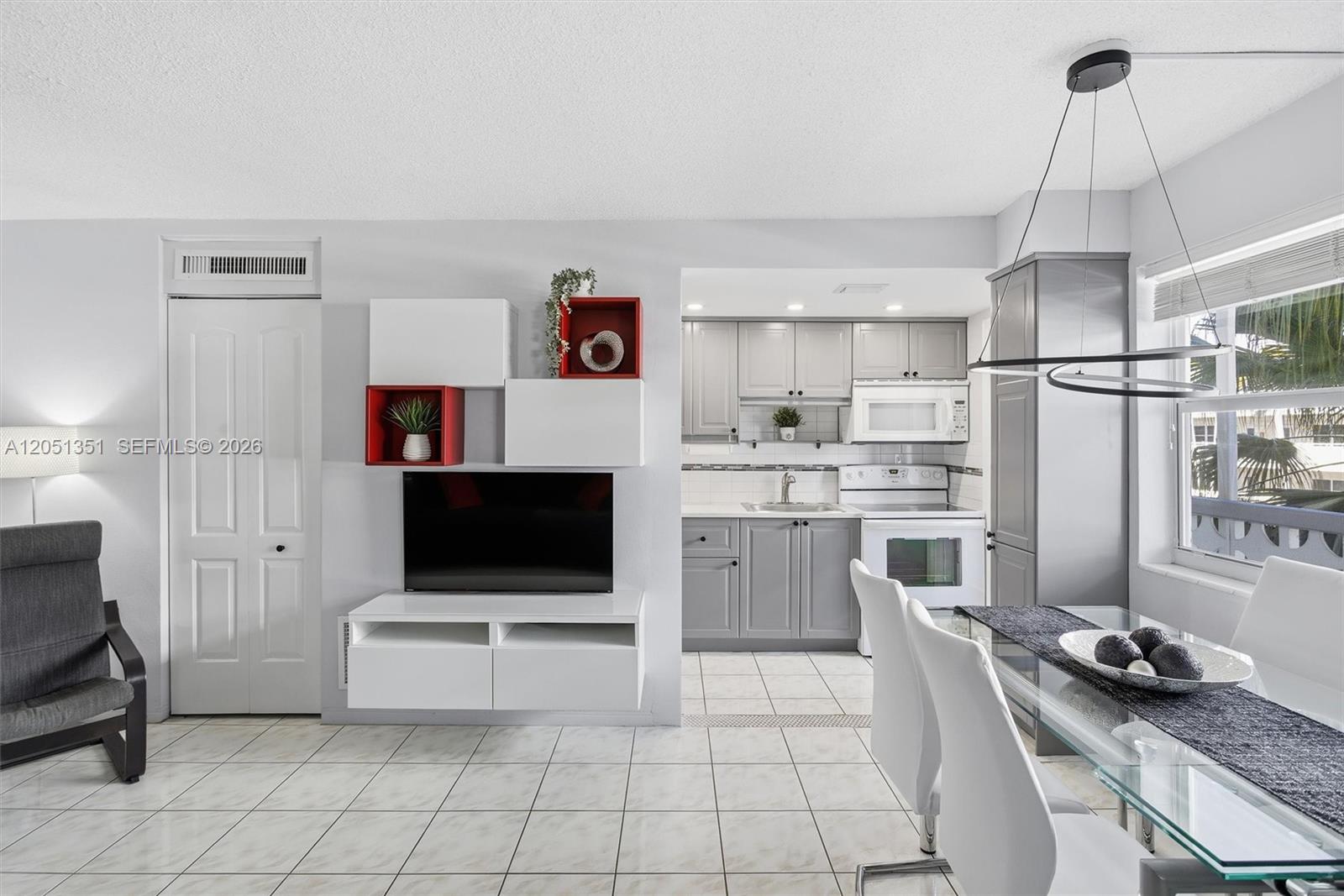 A modern living and dining area features white tile floors, gray cabinetry, and wall-mounted shelving — 3133 S Ocean Dr # 218, Hallandale Beach FL 33009, HALLANDALE BEACH, FL