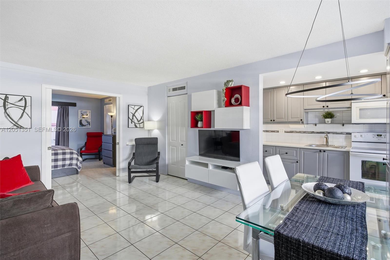 A living room with tiled floors, a wall-mounted TV unit, and an adjacent kitchen — 3133 S Ocean Dr # 218, Hallandale Beach FL 33009, HALLANDALE BEACH, FL
