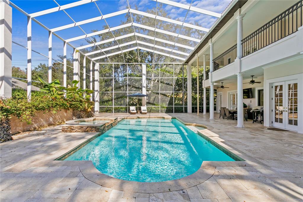 A screened-in swimming pool and spa area with a stone patio and two-story house exterior — 17027 CANDELEDA DE AVILA, TAMPA, FL