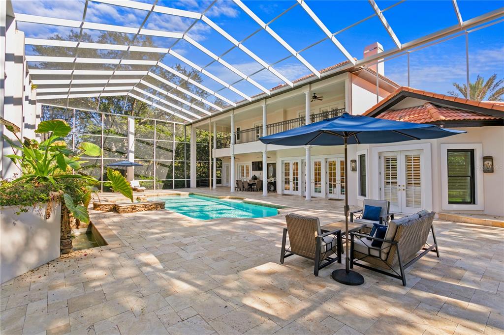 A screened-in patio features a swimming pool, stone pavers, and outdoor furniture under a roof — 17027 CANDELEDA DE AVILA, TAMPA, FL