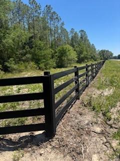 A black four-rail fence runs along the edge of a grassy field near a forest — NE HWY 353, OLD TOWN, FL