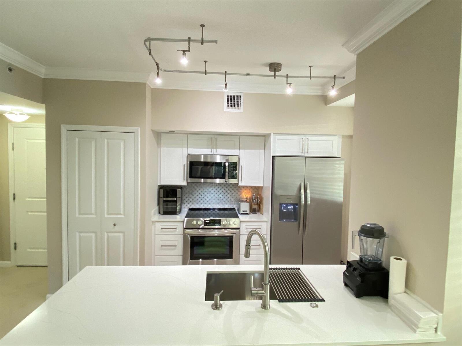 A kitchen features white cabinetry, stainless steel appliances, a quartz island countertop, and track lighting — 225 NE 1st Street # 202, Delray Beach FL 33444, DELRAY BEACH, FL