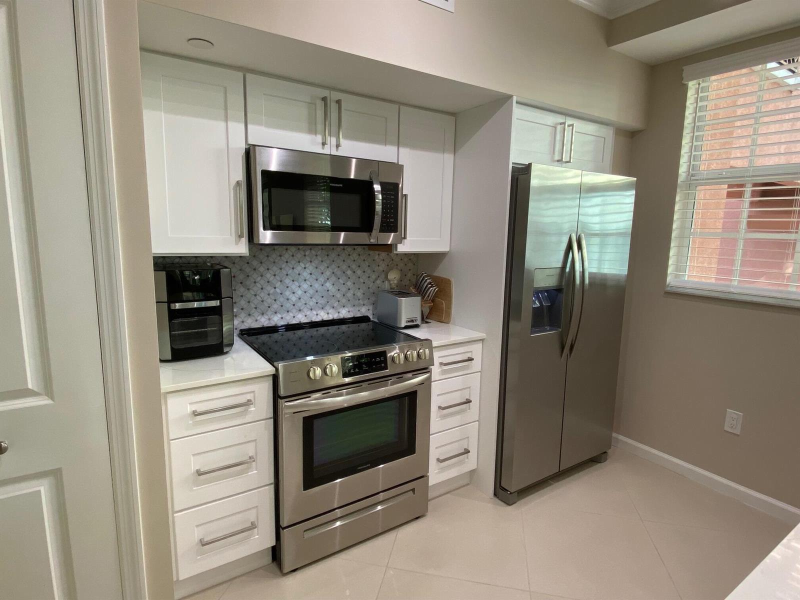 A kitchen featuring white cabinets, stainless steel appliances, a patterned backsplash, and light tile flooring — 225 NE 1st Street # 202, Delray Beach FL 33444, DELRAY BEACH, FL