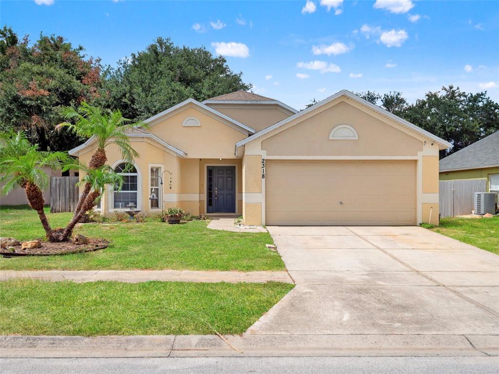A single-story house with a beige stucco exterior, a two-car garage, and a palm tree — 2318 BARONS COURT, TAVARES, FL