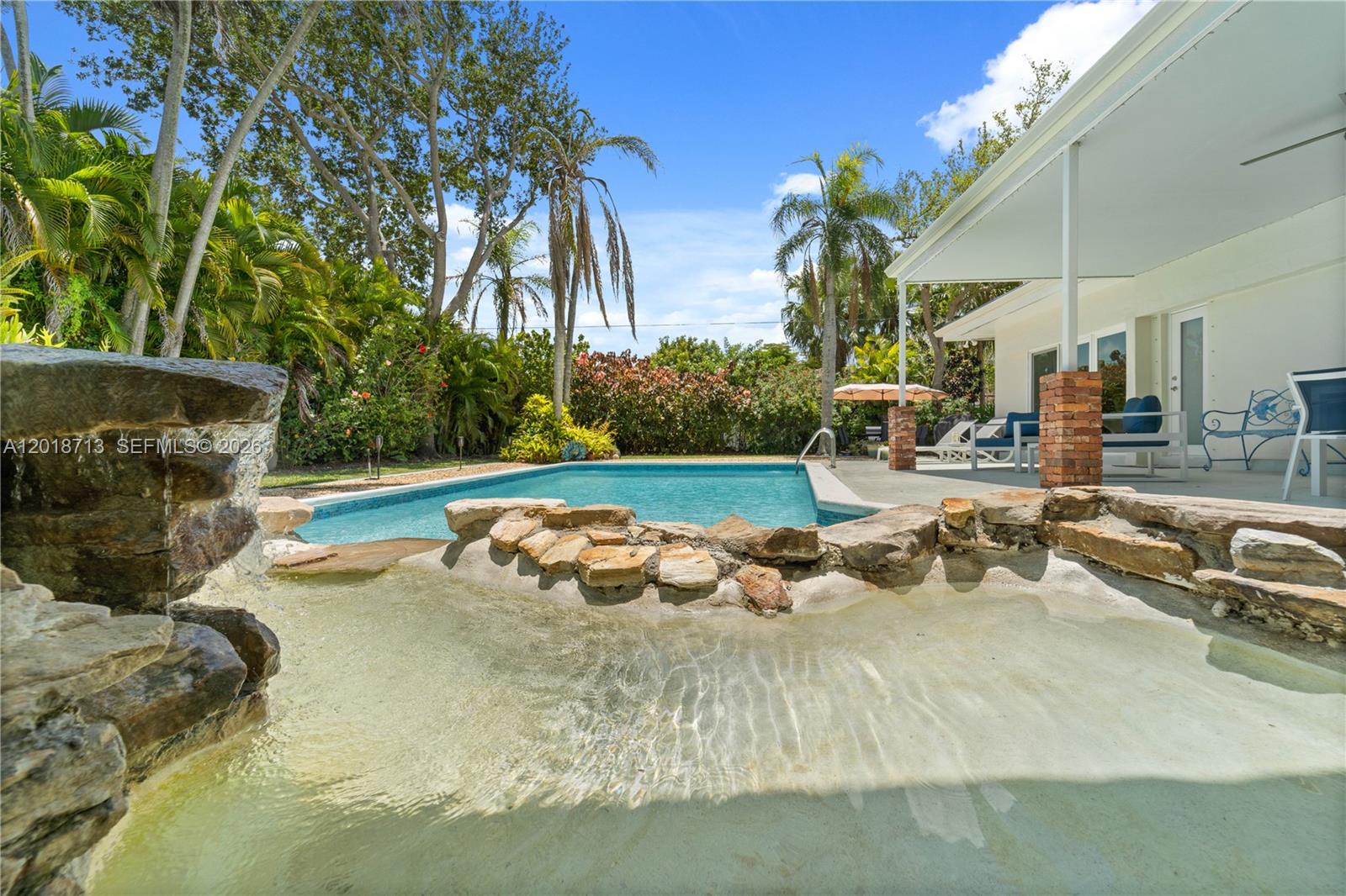 A backyard swimming pool features a stone waterfall and a covered patio area — 8380 SW 186 St, Cutler Bay FL 33157, CUTLER BAY, FL