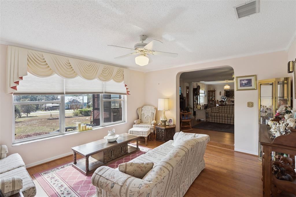 A living room with wood flooring, a ceiling fan, a large window, and patterned furniture — 17530 COUNTY ROAD 455, MONTVERDE, FL