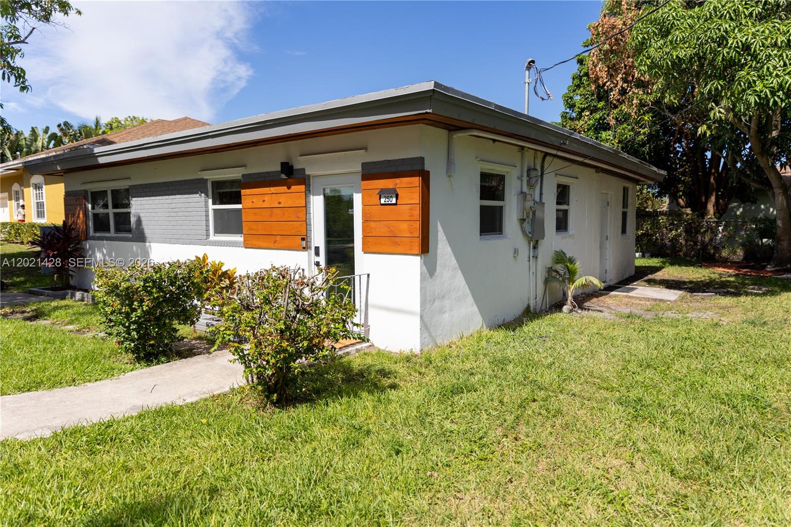 A single-story white house with grey brick accents and wood-paneled shutters around the entrance — 250 NW 14th Way, Dania Beach FL 33004, DANIA BEACH, FL