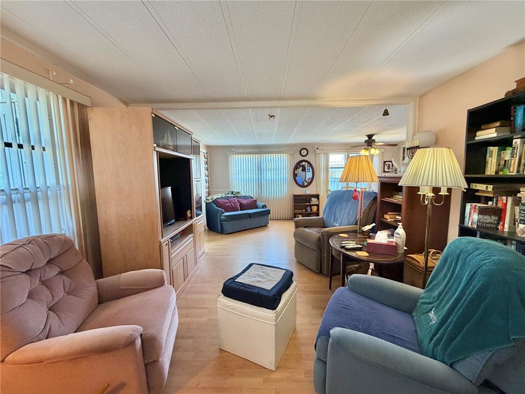 A living room with wood-look flooring, a large entertainment center, and several armchairs — 167 JACARANDA DRIVE, LEESBURG, FL