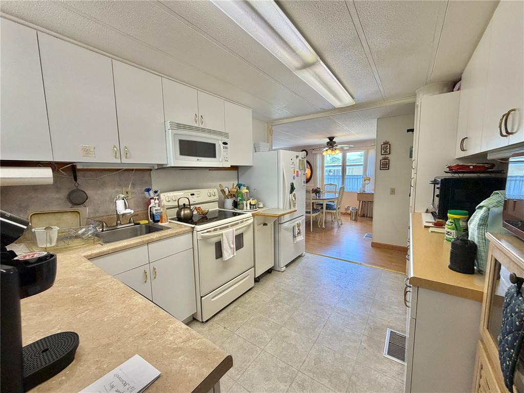 A kitchen with white cabinets, laminate countertops, and white appliances opens into a dining area — 167 JACARANDA DRIVE, LEESBURG, FL