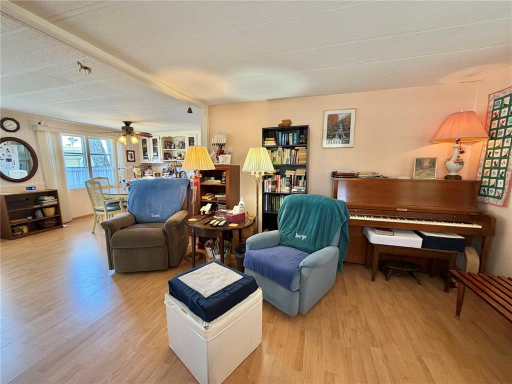 A living room features two armchairs, a piano, a bookshelf, and light wood-look flooring — 167 JACARANDA DRIVE, LEESBURG, FL