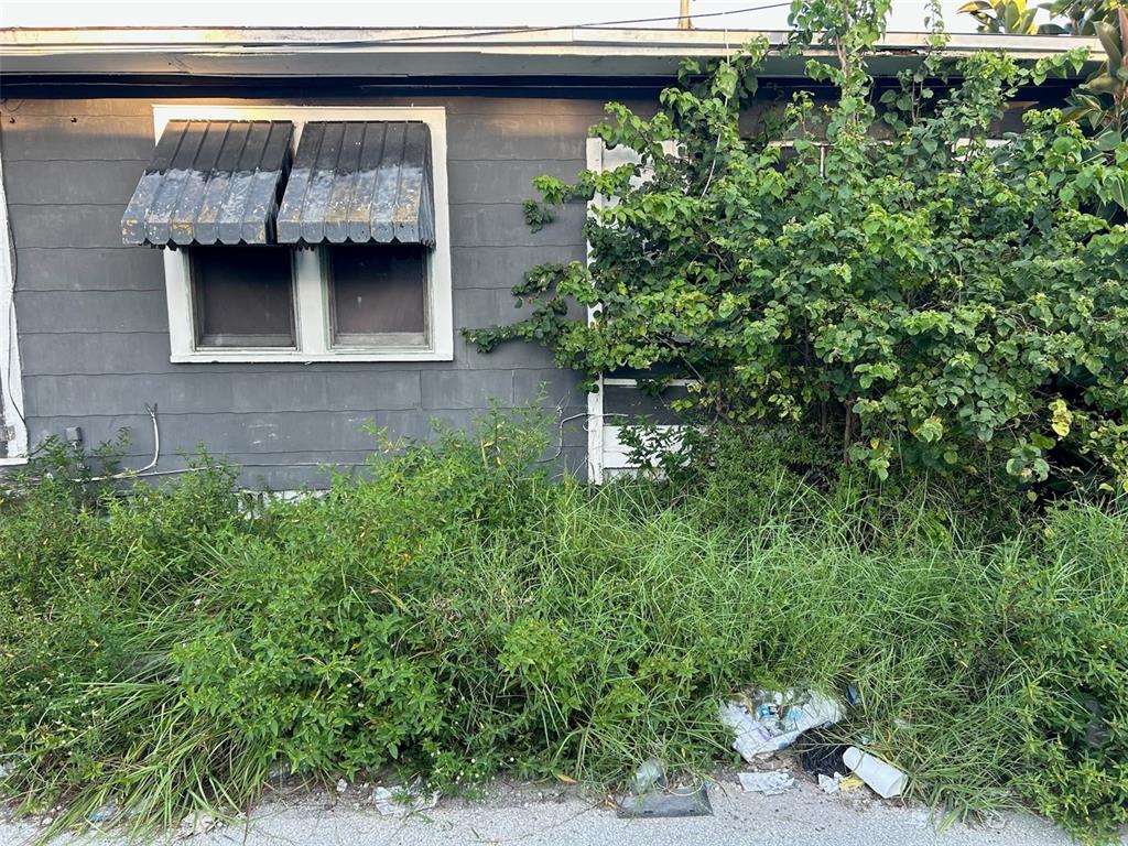 The exterior of a grey house features a window with a metal awning and overgrown vegetation — 877 22ND AVENUE S, ST PETERSBURG, FL