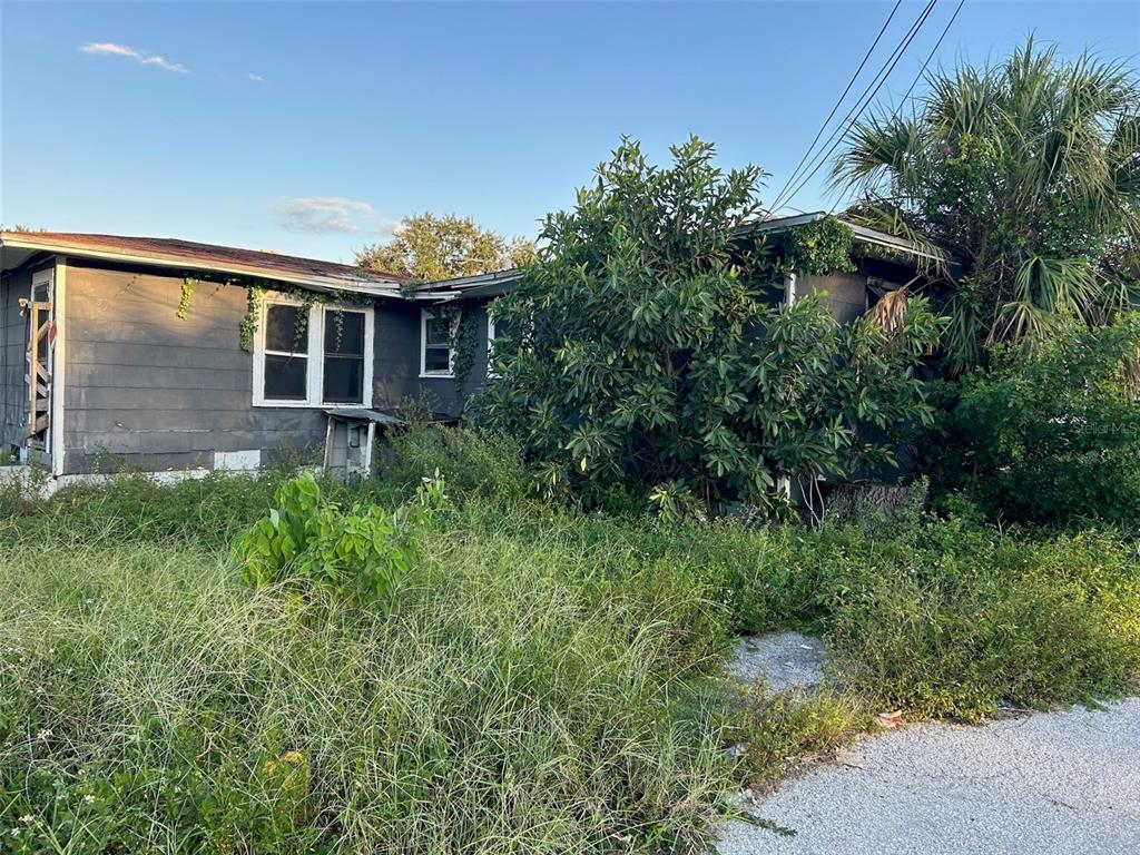 An exterior view of a dilapidated, overgrown single-story house with dark siding and damaged windows — 877 22ND AVENUE S, ST PETERSBURG, FL