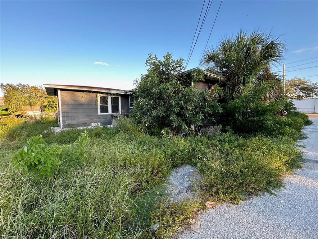 A weathered, single-story house is surrounded by overgrown vegetation and a gravel driveway — 877 22ND AVENUE S, ST PETERSBURG, FL