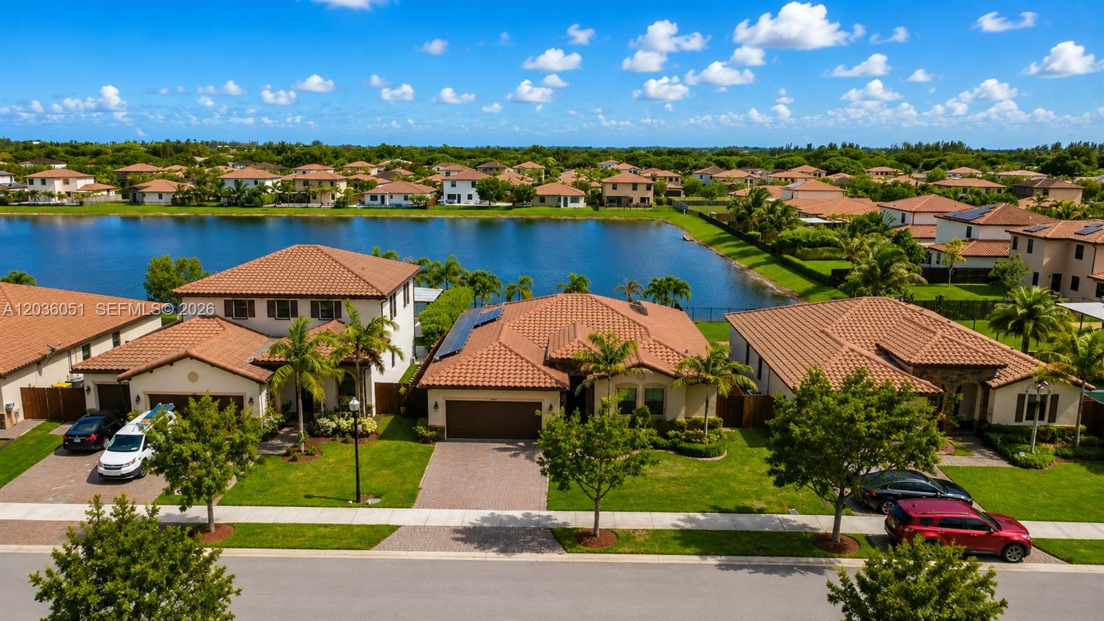 An aerial view shows three suburban houses with tiled roofs situated along a lake — 2450 SE 1st St, Homestead FL 33033, HOMESTEAD, FL