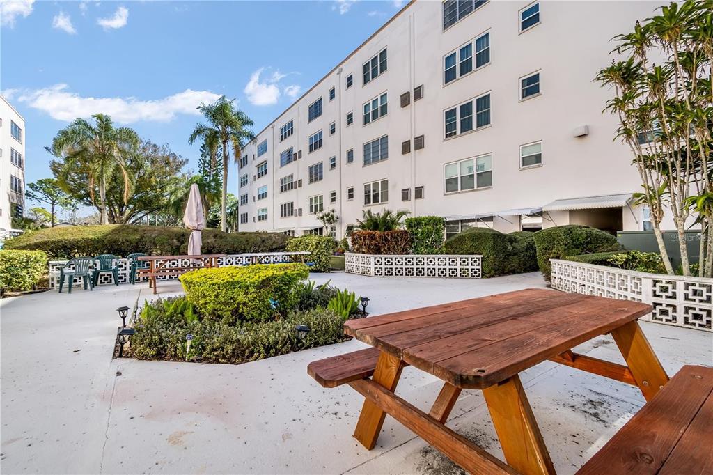 A wooden picnic table sits on a concrete patio outside a multi-story apartment building — 5603 80TH STREET N UNIT 512, ST PETERSBURG, FL