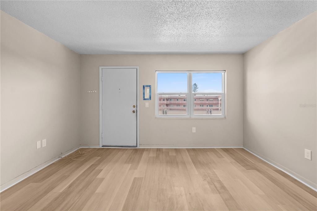 An empty room with light wood-look flooring, a white door, and a window — 5603 80TH STREET N UNIT 512, ST PETERSBURG, FL