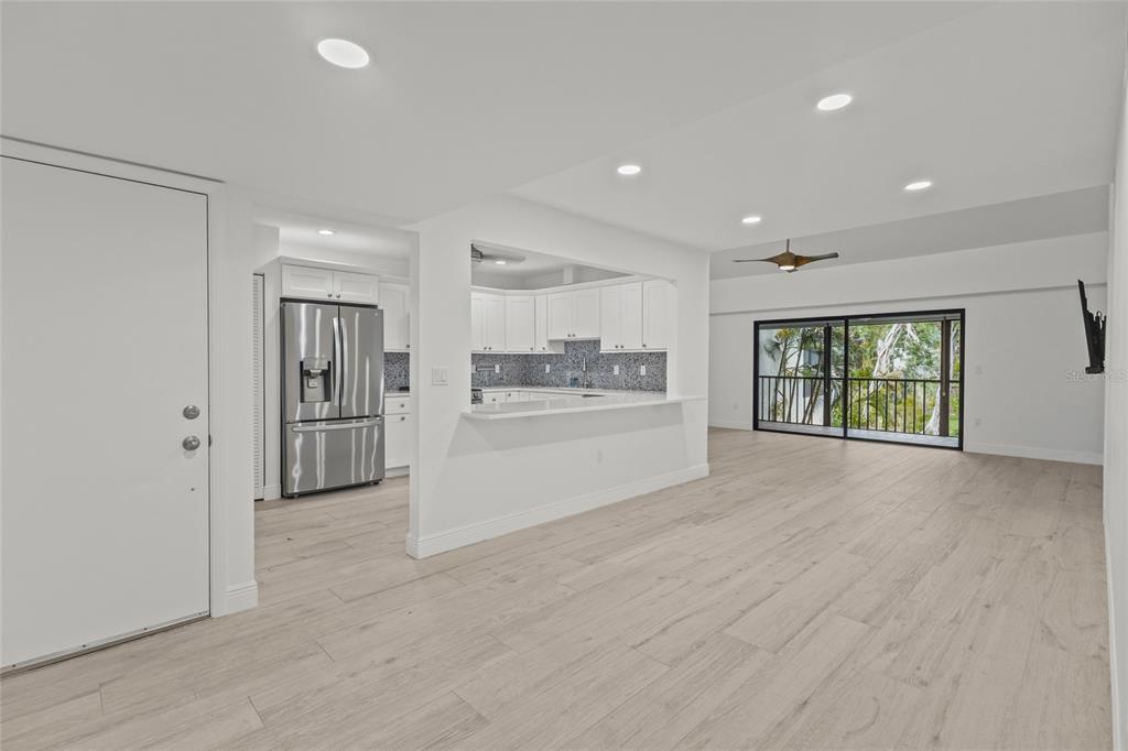 An open-concept living area features light wood-look flooring, a kitchen with white cabinets, and a balcony — 1508 PELICAN COVE ROAD UNIT 235, SARASOTA, FL